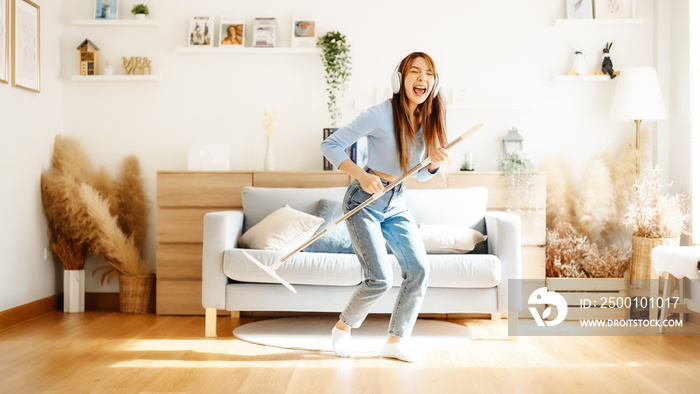 House cleaning with fun. Happy young asian housewife singing her favorite song during cleanup, using mop as microphone, enjoying domestic work. Young woman dancing and cleaning in living room