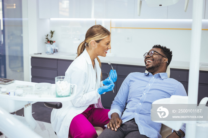 African American young man having a visit at the dentist’s. He is sitting on chair at dentist office in dental clinic.. Happy dentist and patient in dentist’s office. My dentist is the best!