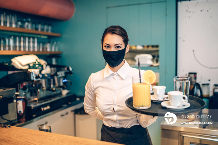 Beautiful young waitress with face protective mask working in cafe bar. Coronavirus or Covid-19 concept.