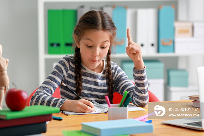 Cute girl with raised index finger doing homework in classroom