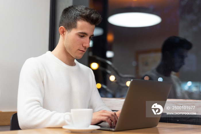 Young man working on his laptop in a coffee shop, young student typing on computer .