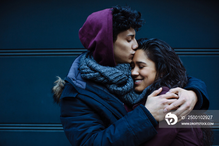 Close up portrait of a happy young hispanic couple embracing each other and kissing on forehead