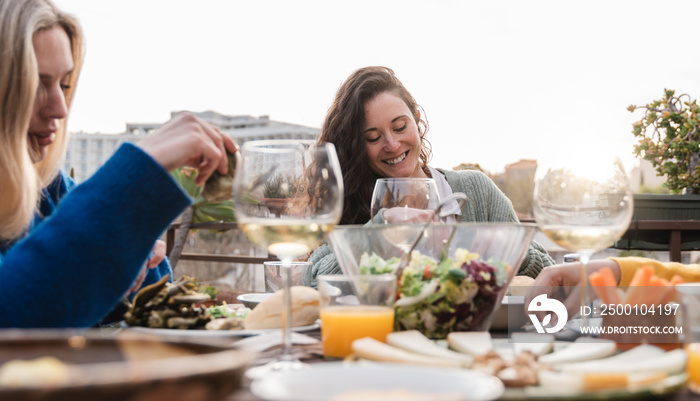 Happy diverse people eating vegan food with wine outdoors in sunset at patio restaurant - Focus on center woman face