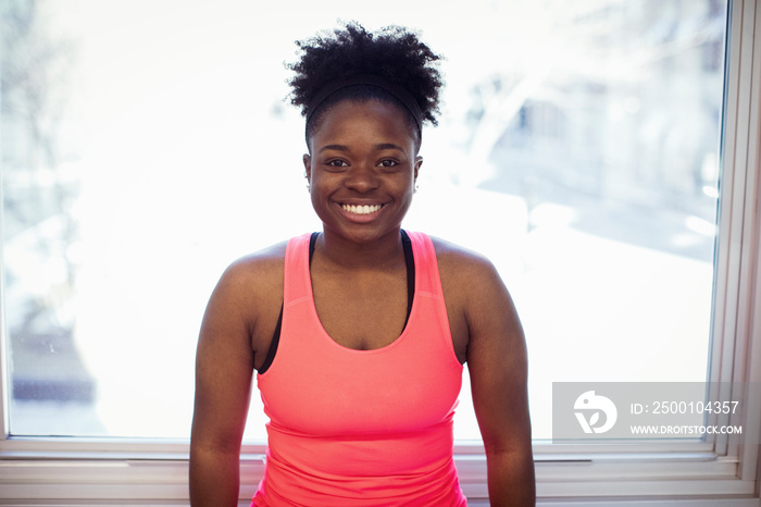 Portrait of happy female athlete standing against window in gym