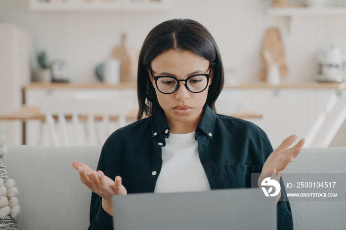 Puzzled woman freelancer in glasses spreading hands, shocked by problems in work, error on laptop