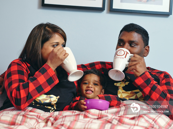 Parents with son drinking and eating in bed