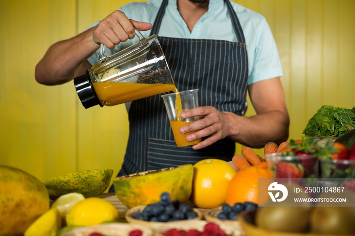 Male staff pouring juice into glass at counter