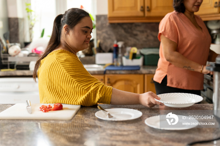 Woman with down syndrome preparing tableware while cooking with mother