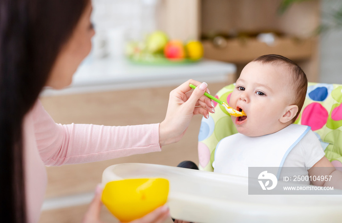 Mother feeding her baby son with porridge at kitchen