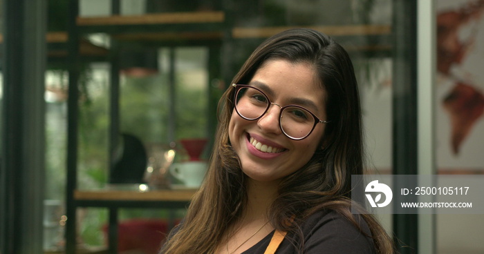 Portrait of young woman employee standing in front of coffee shop smiling at camera