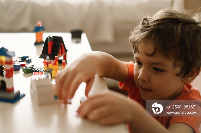 Cute boy is playing constructor at home. Kid playing block toys in home at nursery. Toddler having fun and building out of bright constructor bricks. Development and Construction Concept