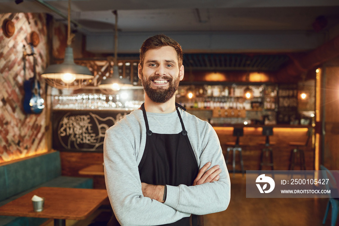 Bearded smiling barman waiter standing on the background of a bar.