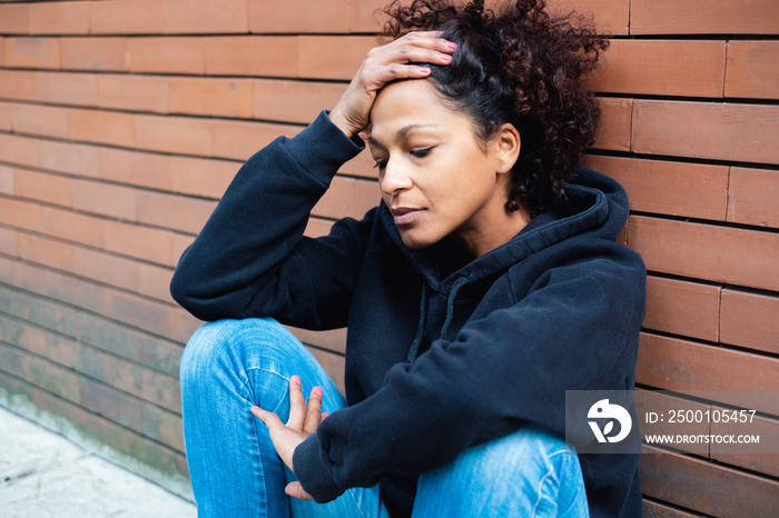 Problematic young woman leaning on brick wall in city street