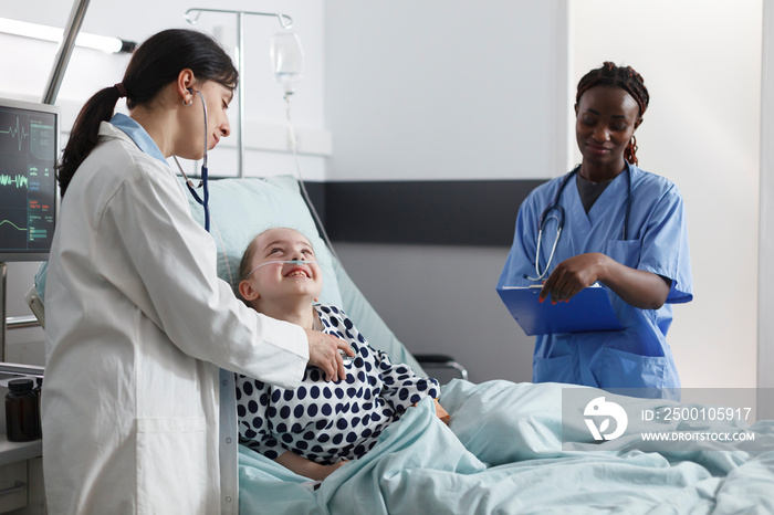 Pediatric clinic general practitioner specialist examining girl health condition using stethoscope. Hospital african american nurse taking consultation results notes while in medical patient room.