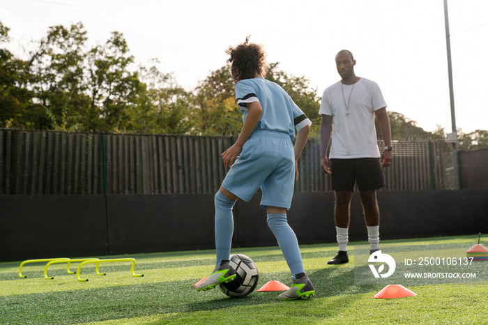 Coach watching girl (6-7) practicing on soccer field