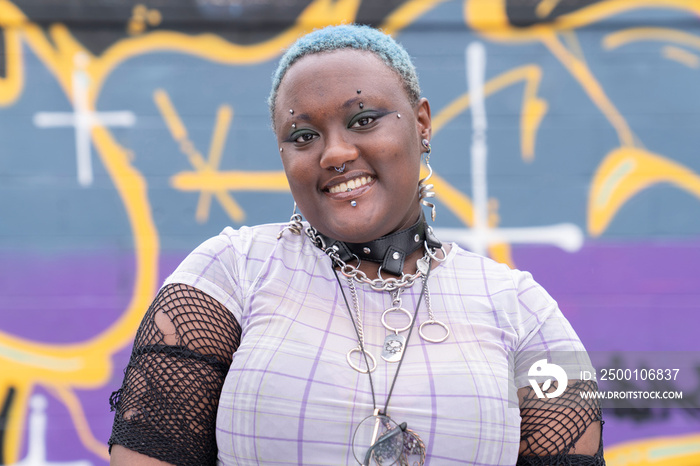 Portrait of smiling non-binary person against graffiti wall