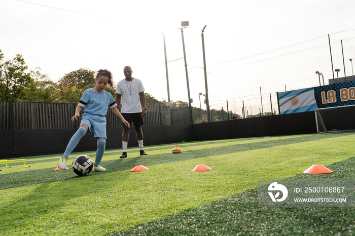 Coach watching girl (6-7) practicing on soccer field