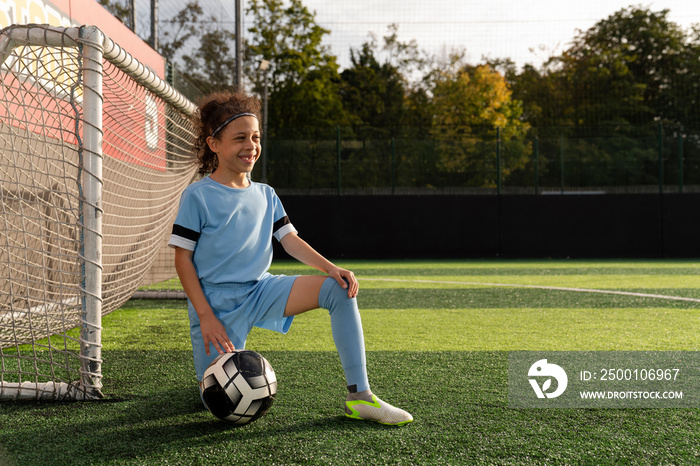 Portrait of girl (6-7) with ball next to soccer goal