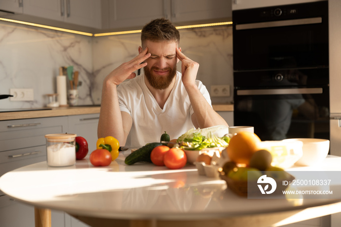 Young tired man with headache sitting at table