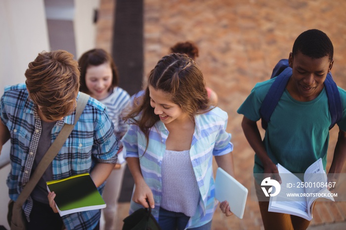 Students holding books and digital tablet walking through school campus