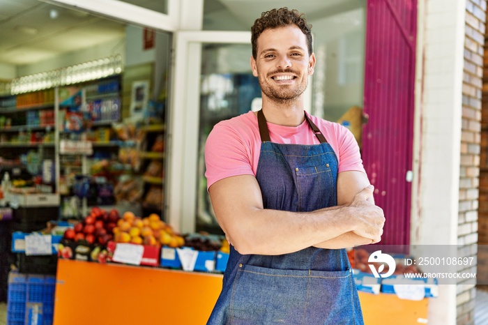 Young hispanic worker wearing apron standing with arms crossed gesture at the fruit store.