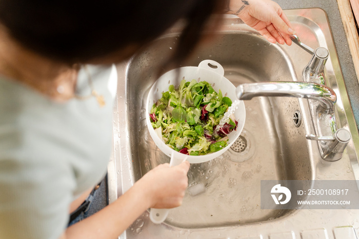 Young woman washing food in kitchen sink