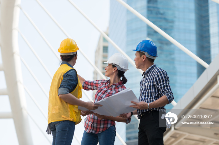 Asian engineers group consult construction on site building working while holding blueprint paper. in city background. teamwork concept.