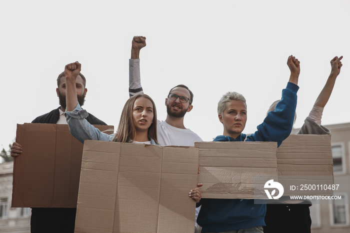 Human rights. Group of activists giving slogans in a rally. Caucasian men and women marching together in a protest in the city. Look angry, hopeful, confident. Blank banners for your design or ad.