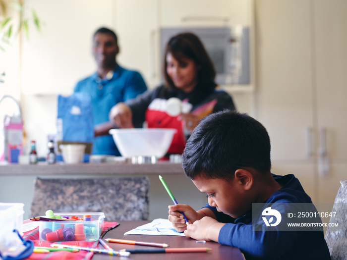 Boy drawing at table while parents cooking