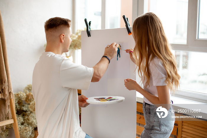 Young couple drawing together. Wife and husband painting on canva and holding brush and pallette with colors.