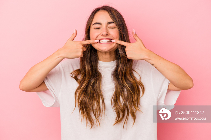 Young caucasian woman isolated on pink background smiles, pointing fingers at mouth.