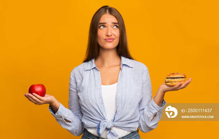 Girl Choosing Between Burger And Apple Standing Over Yellow Background