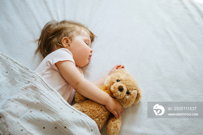 Little baby sleeping on bed embracing soft toy, free space