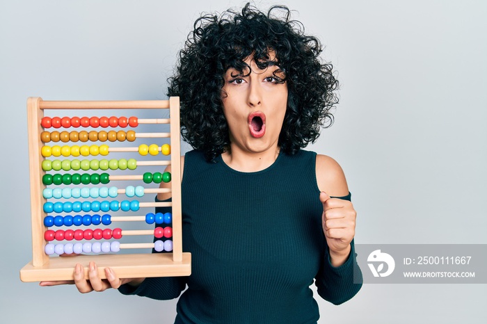 Young middle east woman holding traditional abacus scared and amazed with open mouth for surprise, disbelief face