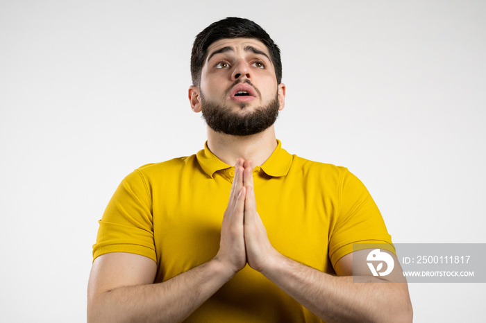 Young caucasian man praying over white background. Guy begging someone satisfy his desires, help with.