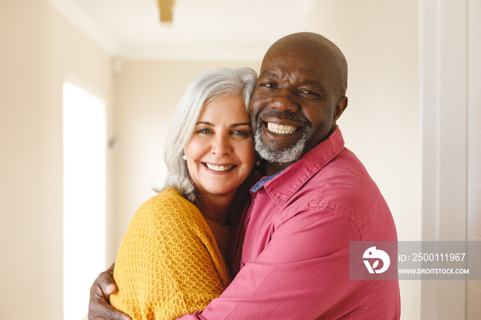 Portrait of happy diverse senior couple embracing and smiling to camera at home