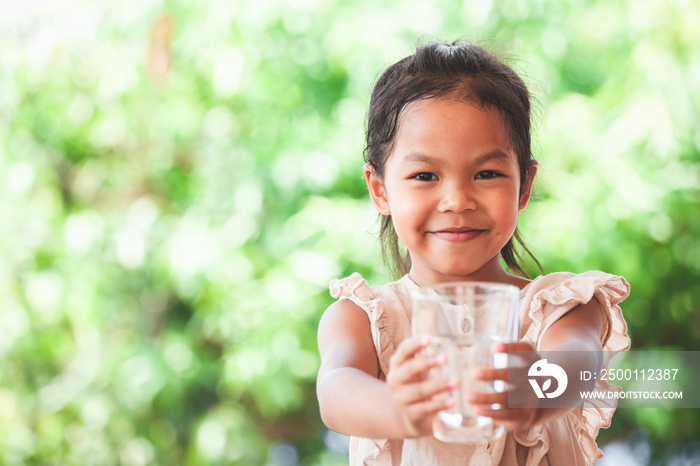 Cute asian child girl like to drink water and holding glass of fresh water in green nature background