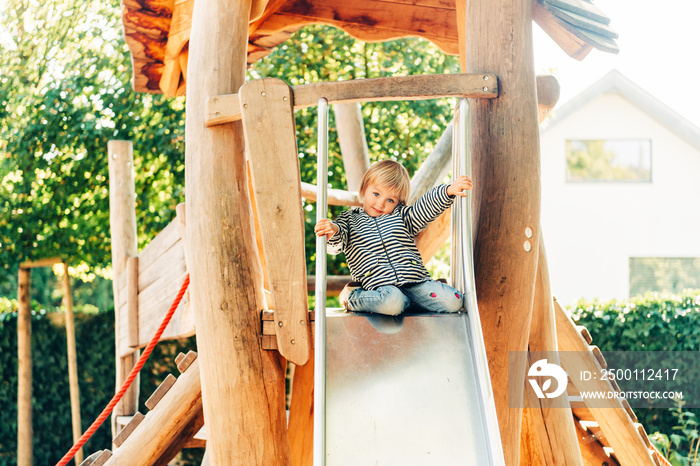 Outdoor portrait of happy toddler girl playing on playground, active child having fun in kids park