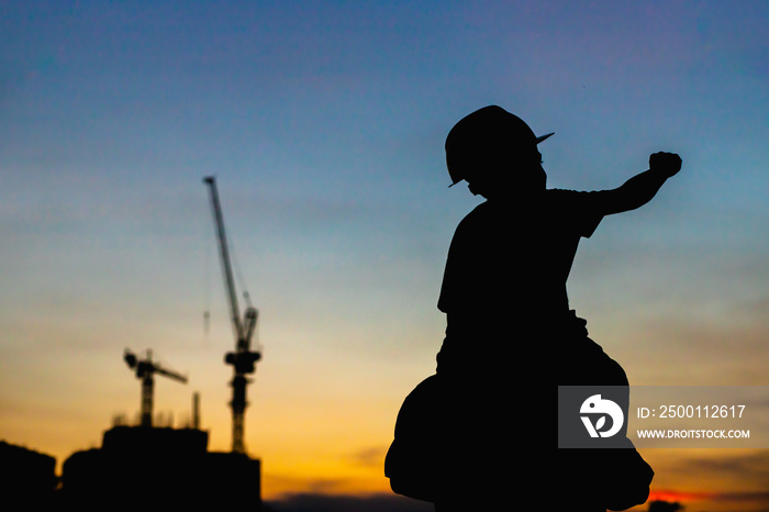 The silhouette of the happy father and son wearing a construction helmet holding hands expressing the joy of the sunset