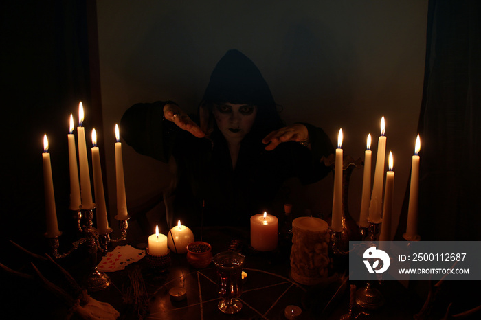 Female Fortuneteller conjures in a dark room, candles are burning on a round esoteric table with a pentagram, animal skulls lie, the concept of magic, witchcraft