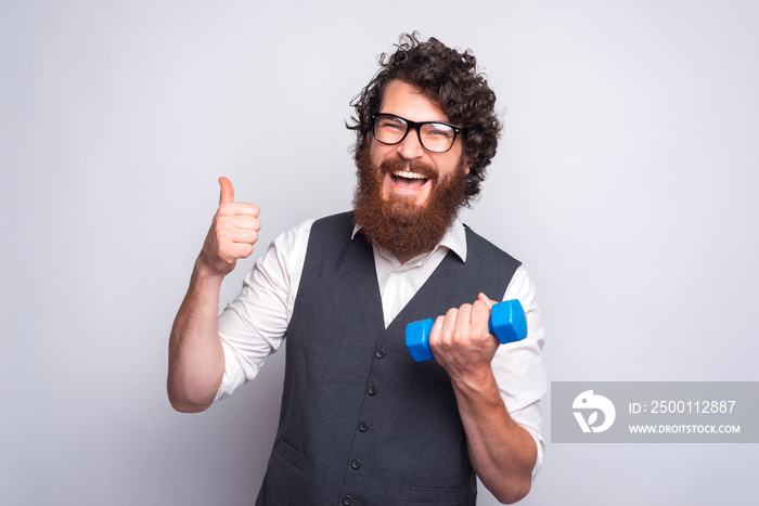 Photo of joyful bearded man in casual working with small dumbbell.