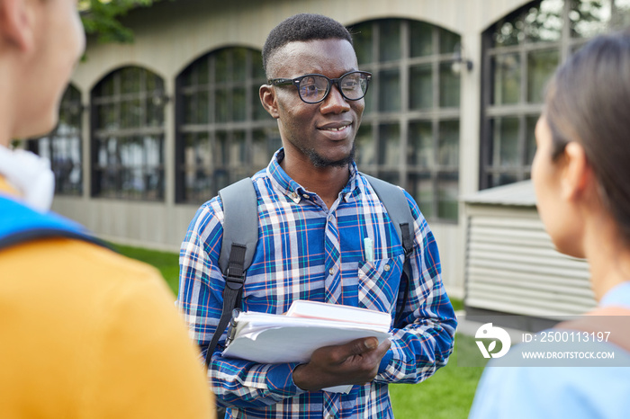 Waist up portrait of cheerful African-American student talking to friends outdoors in college campus, copy space