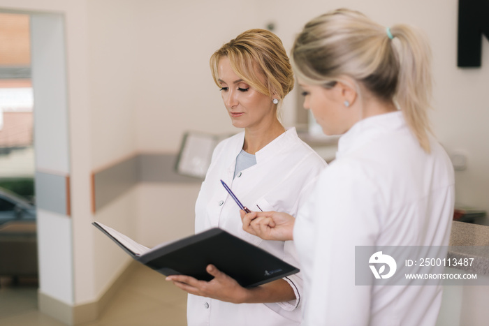 Two good-looking young woman doctor looking at clipboard while standing in the corridor next