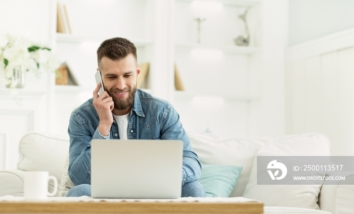 Young man using laptop having phone conversation at home