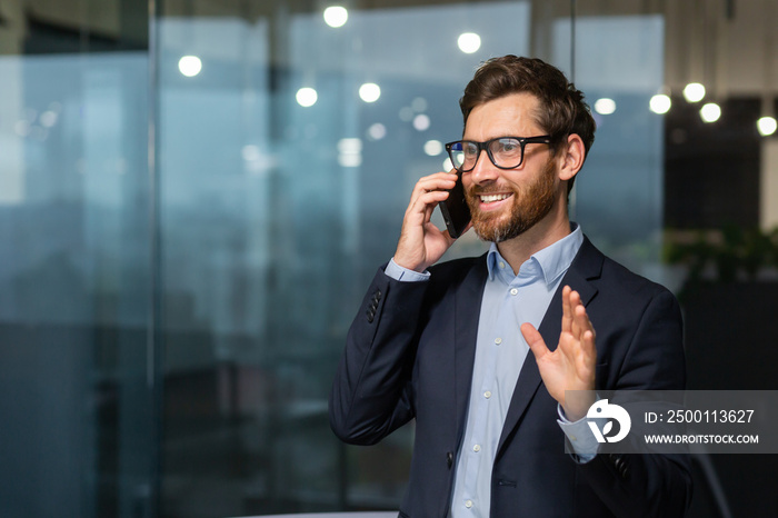 Mature businessman in a business suit talking on the phone, the manager is satisfied with the result of the achievement and work talks about the positive result, the man is at work inside the office.