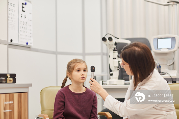 Portrait of female optometrist using tools while checking eyesight of little girl in modern ophthalmology clinic, copy space