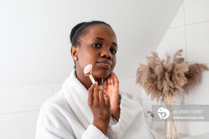 Smiling young woman looking at camera massaging skin by roller