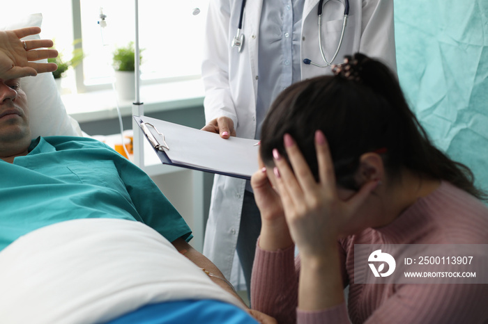 Doctor holding documents in front of crying wife and patient in hospital room