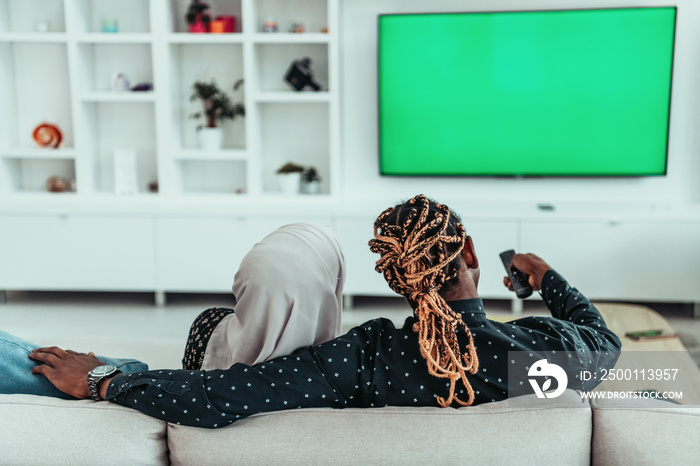 African Couple Sitting On Sofa Watching TV Together Chroma Green Screen Woman Wearing Islamic Hijab Clothes