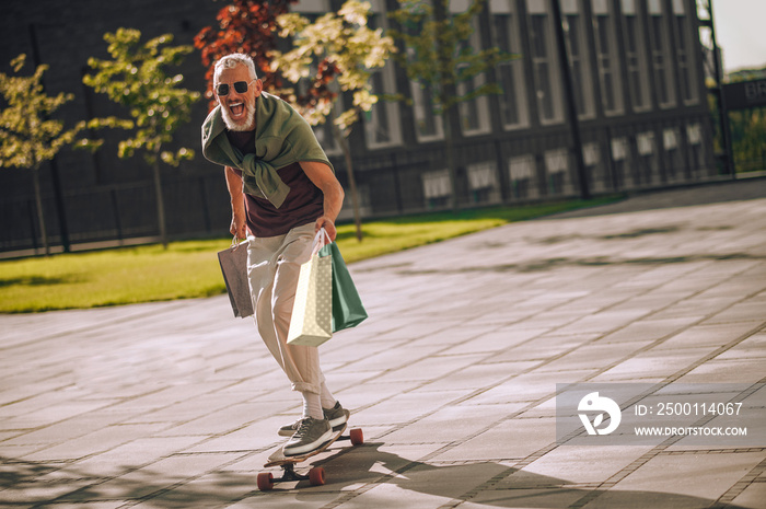 Excited gray-haired bearded Caucasian man skateboarding outside